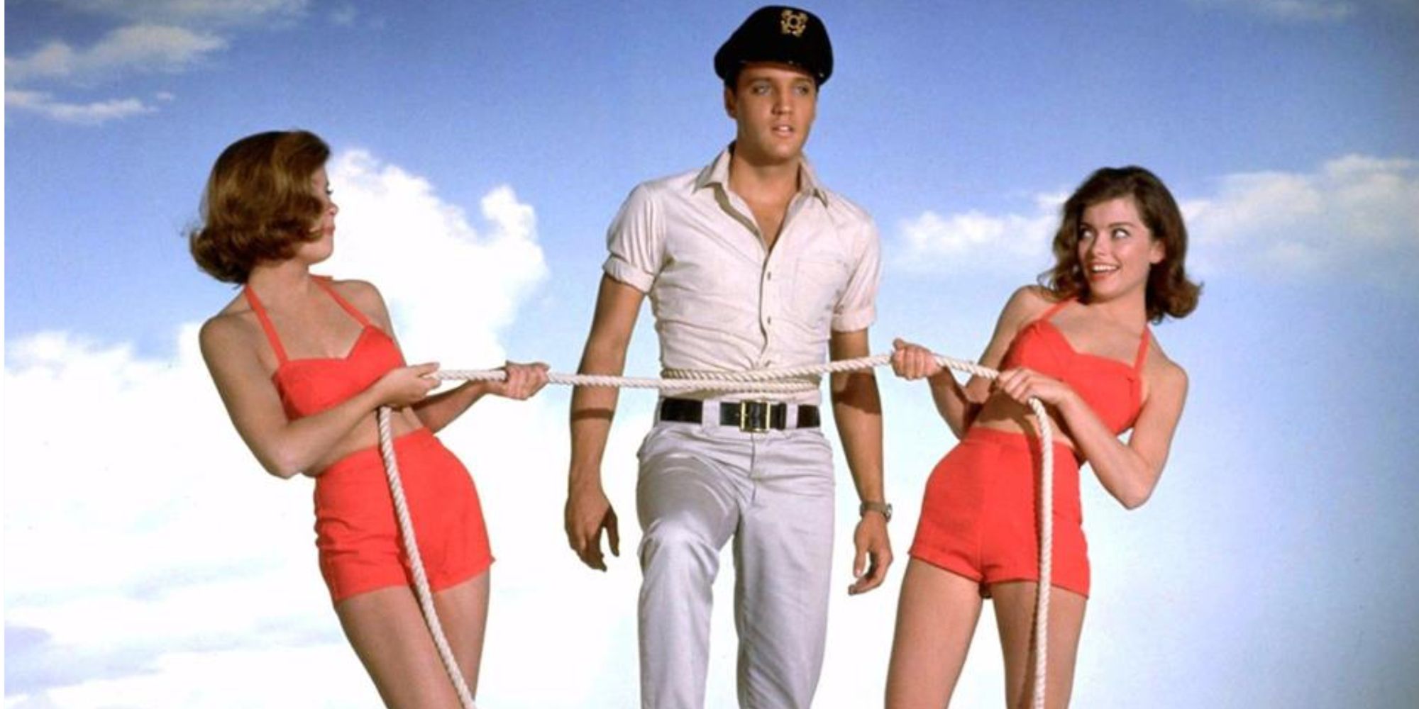 Elvis Presley with a Captain's hat on and two girls tugging at a rope in front of him