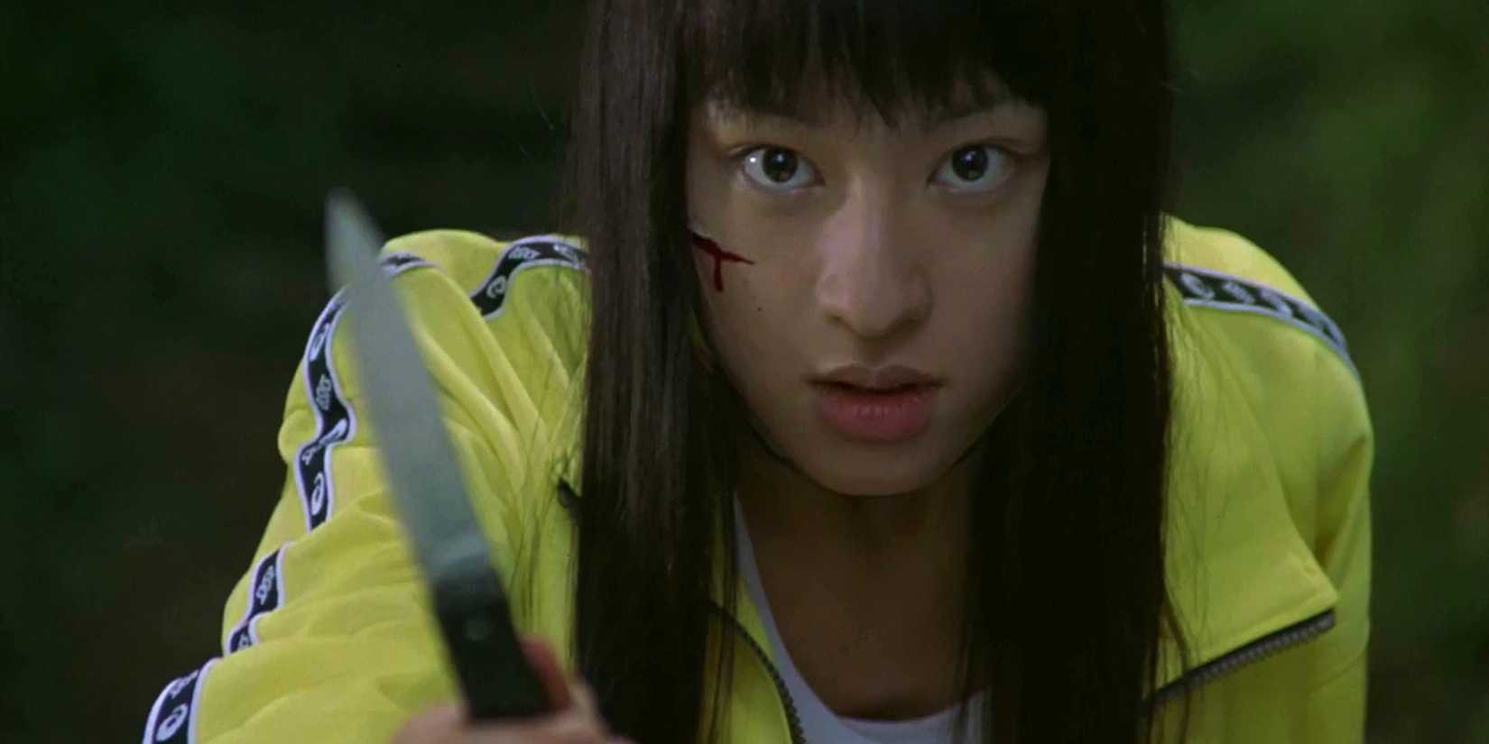 A girl in a yellow tracksuit holding a knife in Battle Royale
