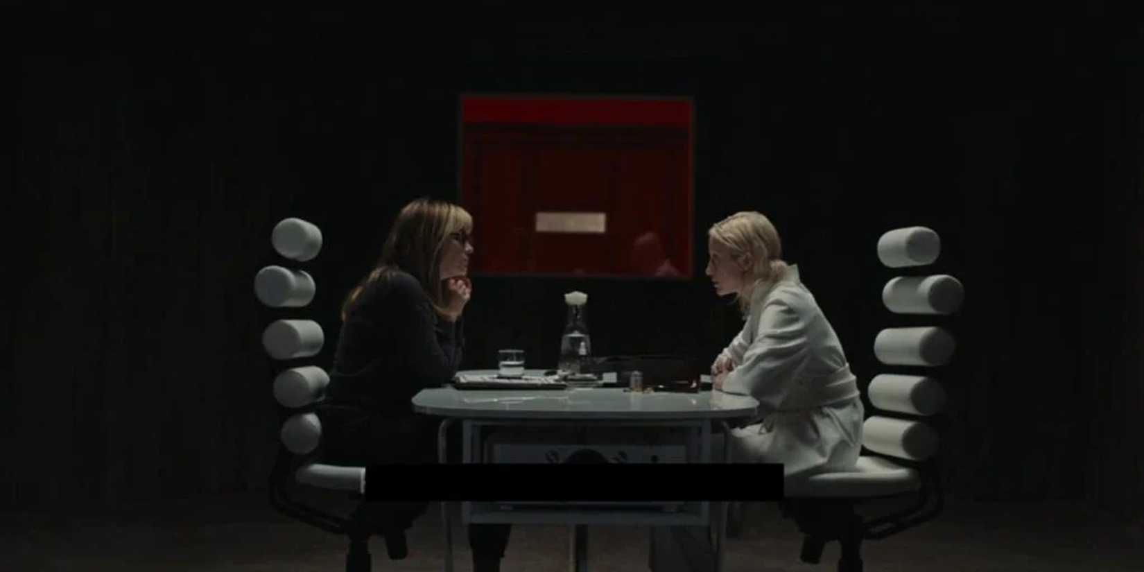 Two women have a conversation across a sleek table in a dark room