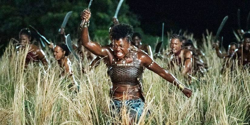 Nanisca raising a weapon and screaming while other female warriors imitate her in The Woman King