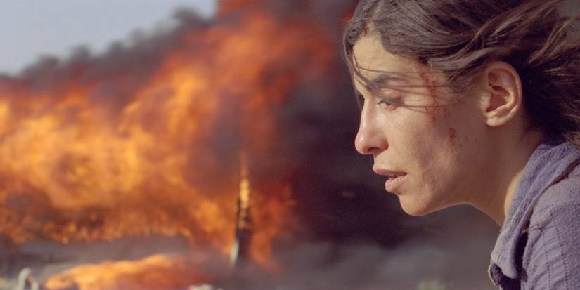A woman looking distraught while a fire burns behind her in Incendies.