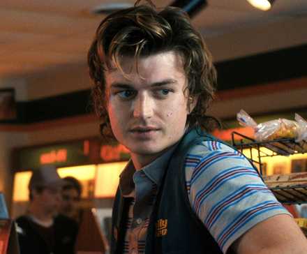 Joe Keery as Steve Harrington at a grocery store looking back at something off-camera in Stranger Things.