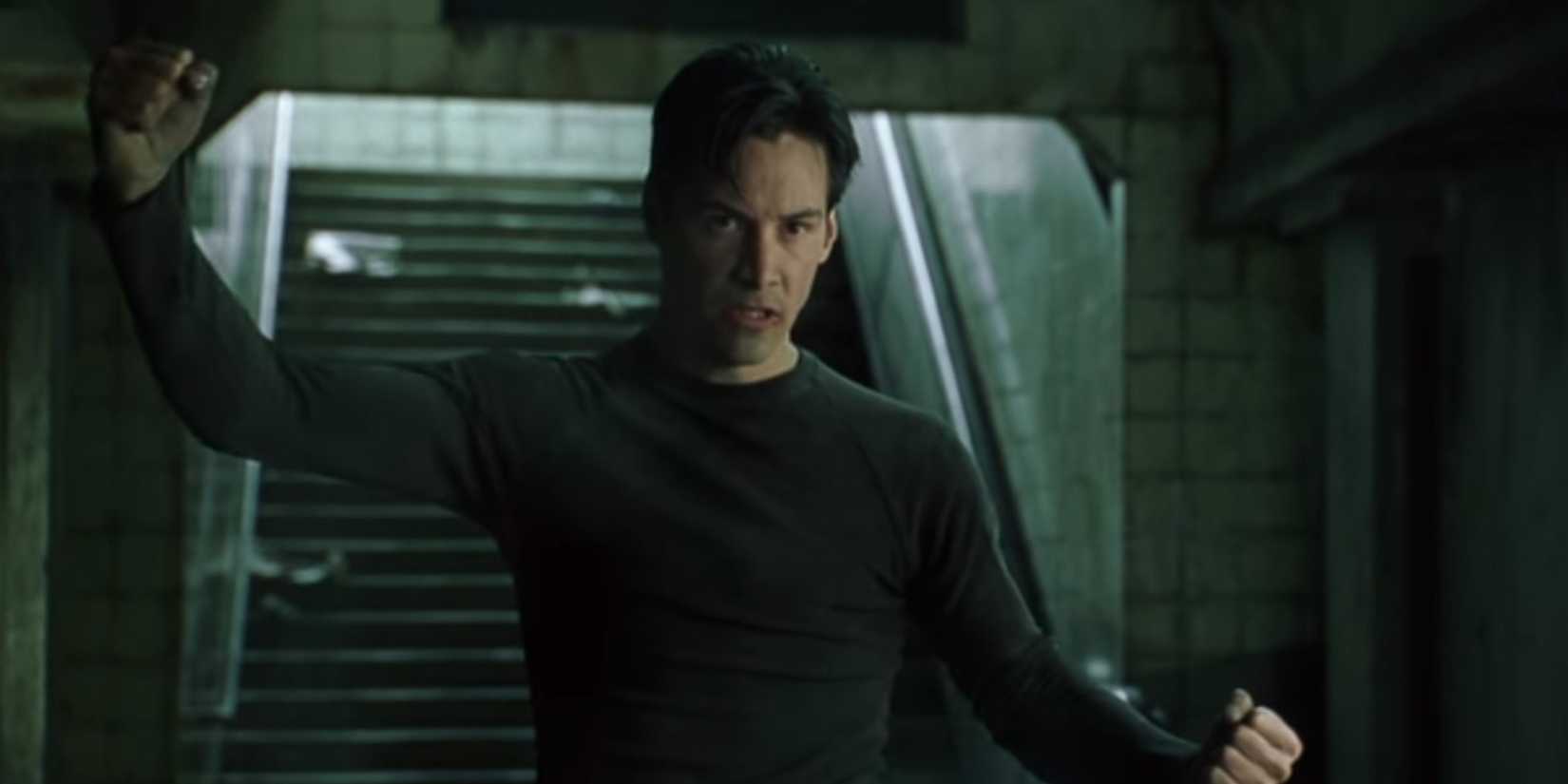 Keanu Reeves flexes his arms in a subway tunnel and prepares to fight in The Matrix.