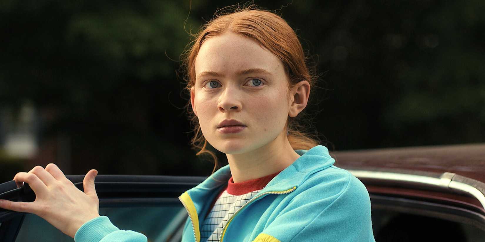 Sadie izlietne kā Makss Meilfīlds Stranger Things 4. sezonā izskatās saspringts netālu no automašīnas ar atvērtām durvīm.