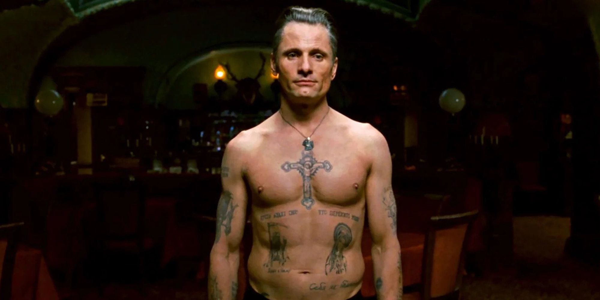 Viggo Mortensen, shirtless, covered in tattoos looking intently at something in Eastern Promises.