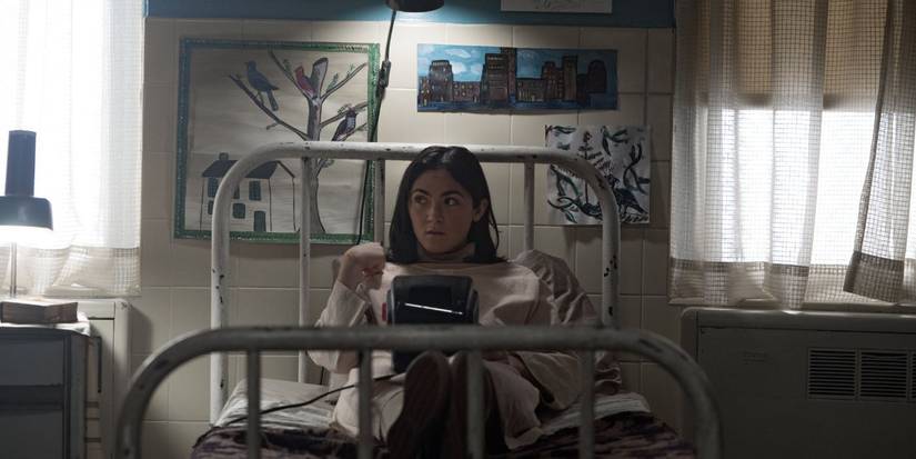 a young girl sits in a shabby bed with children's artwork behind her