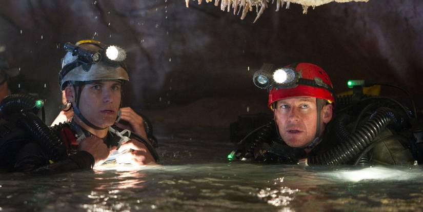 Two cave-diving men in full scuba gear bob at the water's surface inside a cavern