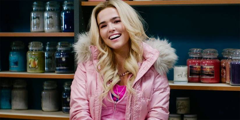 Zoey Deutch in a pink puffer jacket smiles in front of a shelf full of candles in Zombieland: Double Tap.