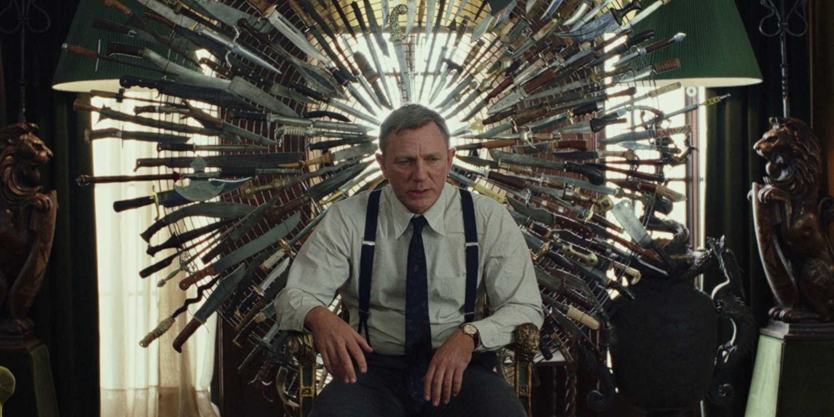 Daniel Craig sitting in a chair in front of a large circular display of knives in Knives Out.