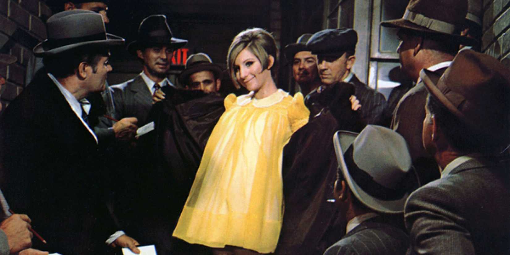 Barbra Streisand as Fanny Brice smiling in a bright yellow dress while surrounded by men in Funny Girl.