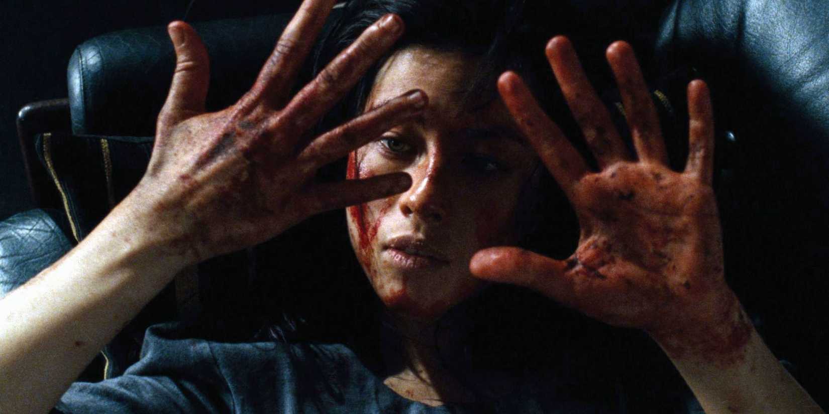 A girl looking at her bloodied hands while lying down on a dark sofa