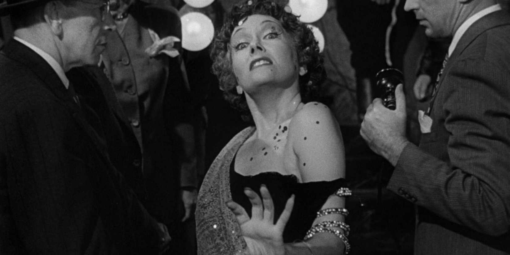 Norma Desmond (Gloria Swanson) glides past Paprazzi, looking intensely at the camera in Sunset Boulevard