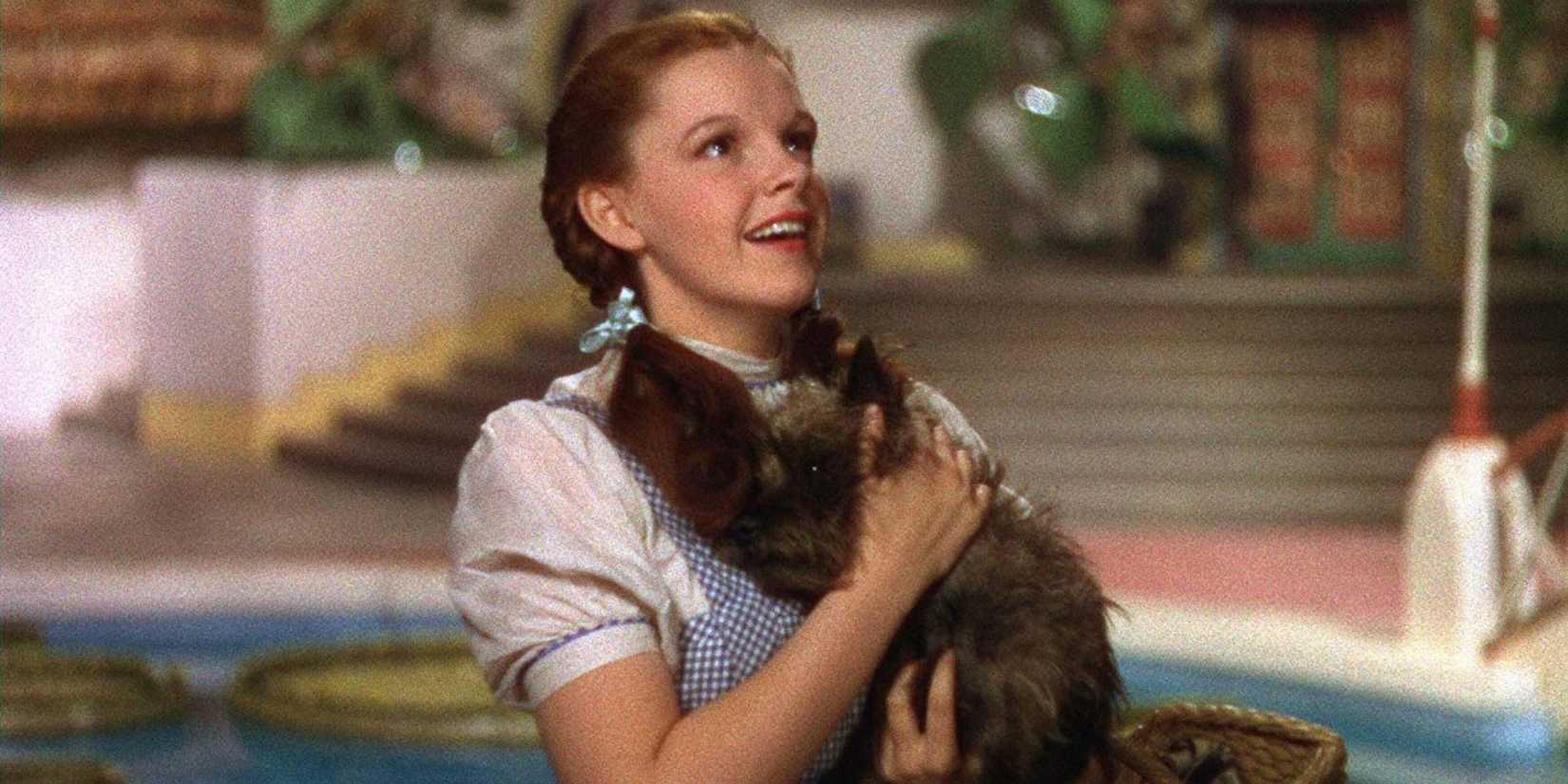 Dorothy, played by Judy Garland, holds Toto while smiling in 'The Wizard of Oz'.