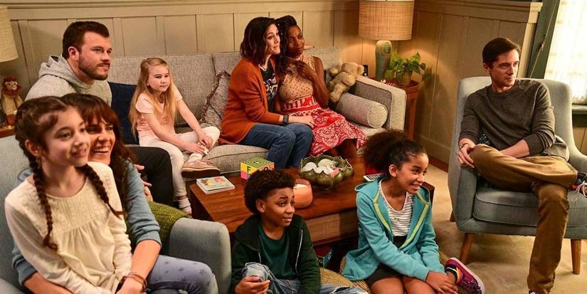 The three siblings and their families from Home Economics sitting around a couch watching TV.