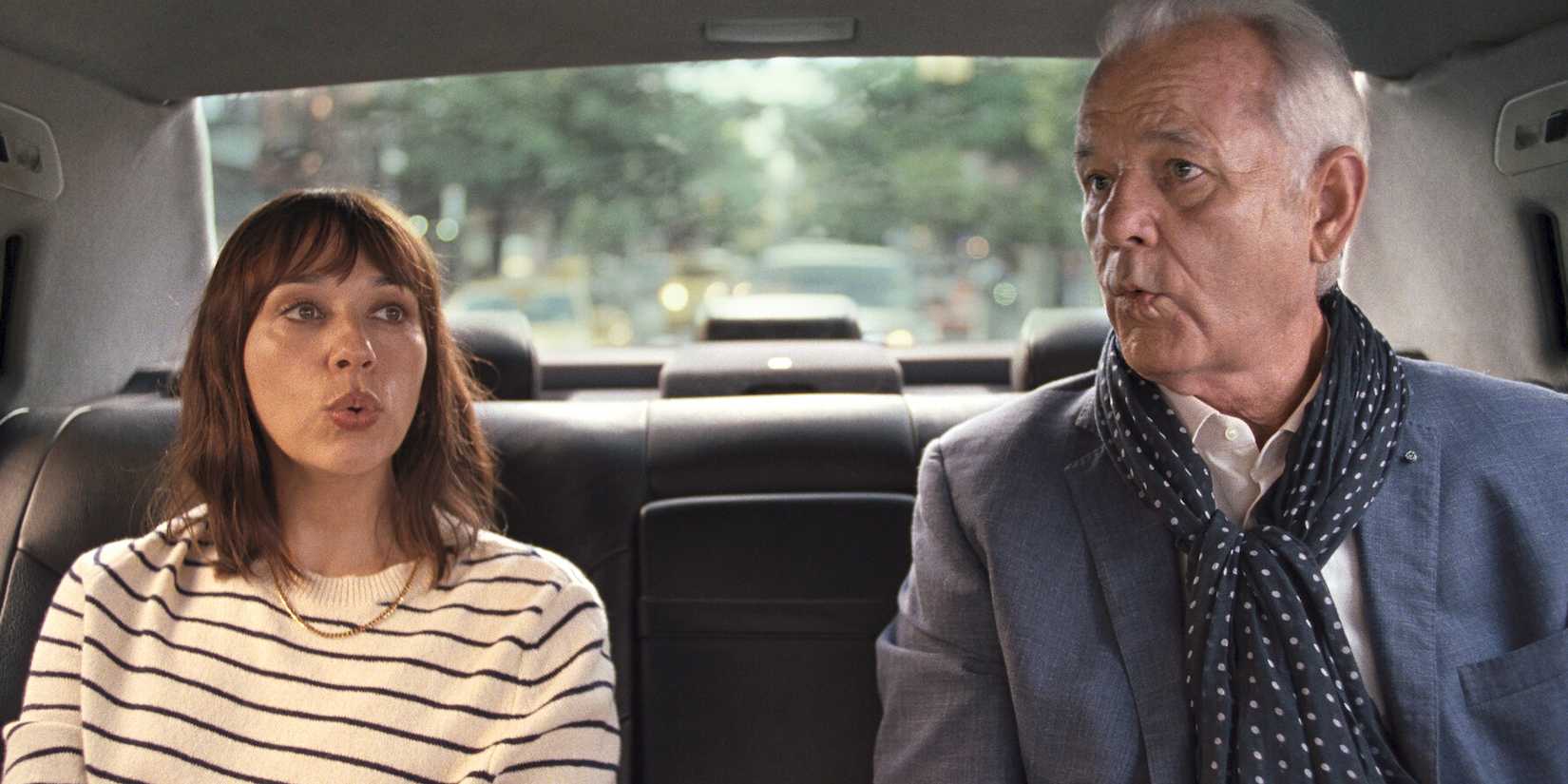 Rashida Jones and Bill Murray in On the Rocks sitting next to each other on a car and whisteling.