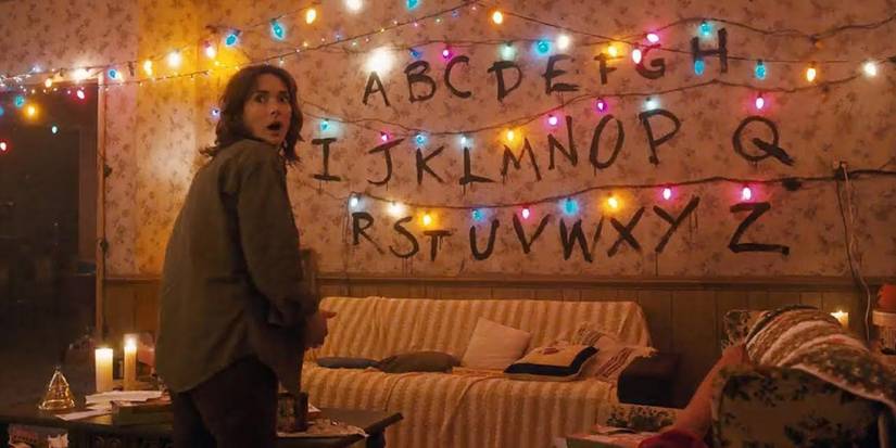 Winona Ryder as Joyce in front of the alphabet written on her wall with Christmas lights in Stranger Things.