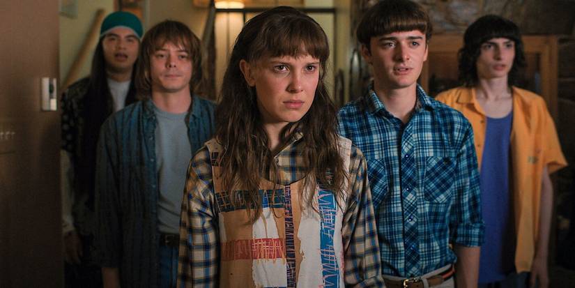 Eleven flanked by her friends, all looking at something off camera seriously, in Stranger Things