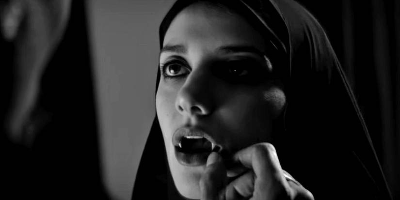 A young woman opens her mouth to reveal vampire fangs in A Girl Walks Home Alone At Night