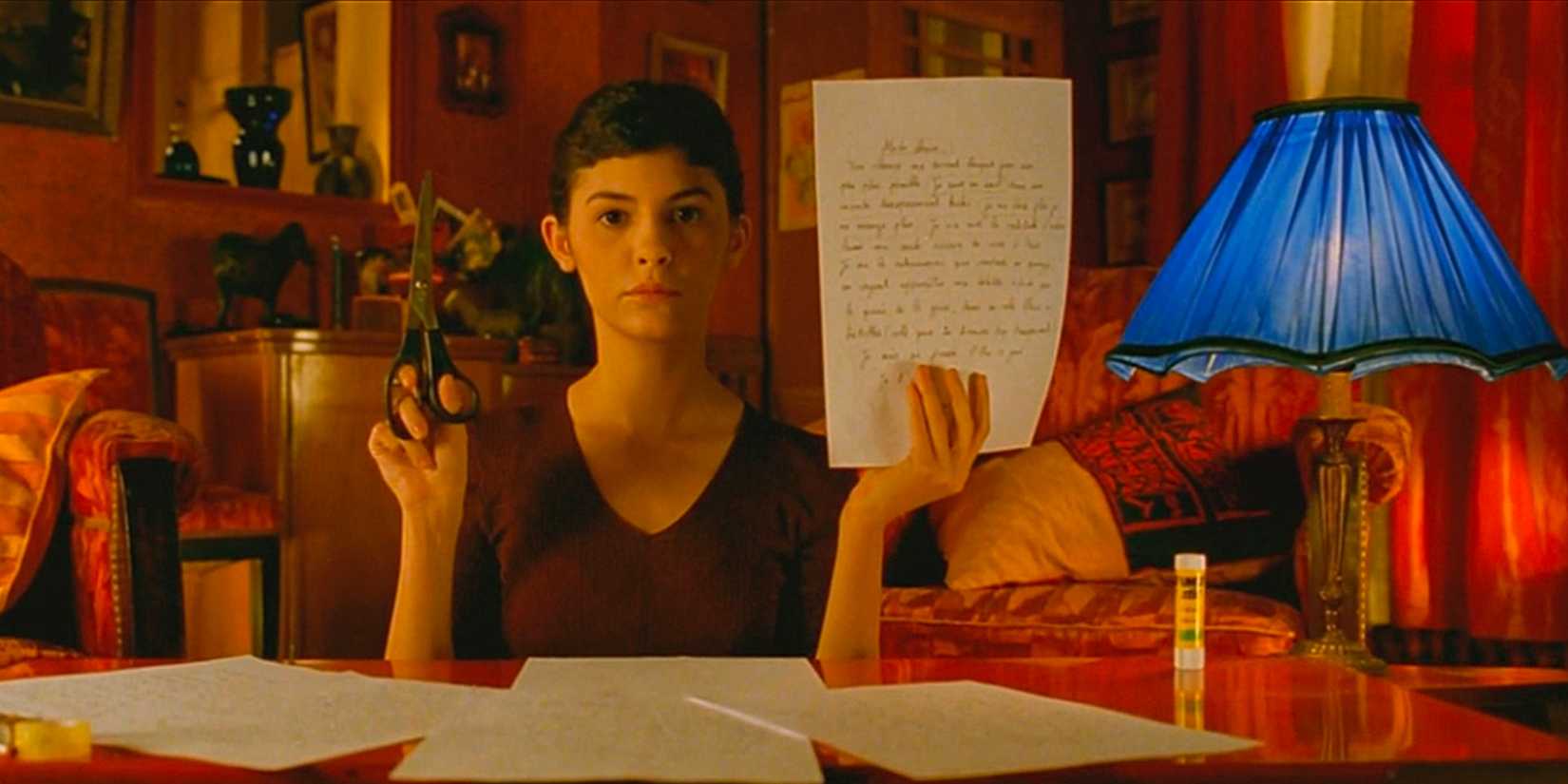 Audrey Tautou holds a paper in one hand and scissors in the other while staring ahead in Amélie.