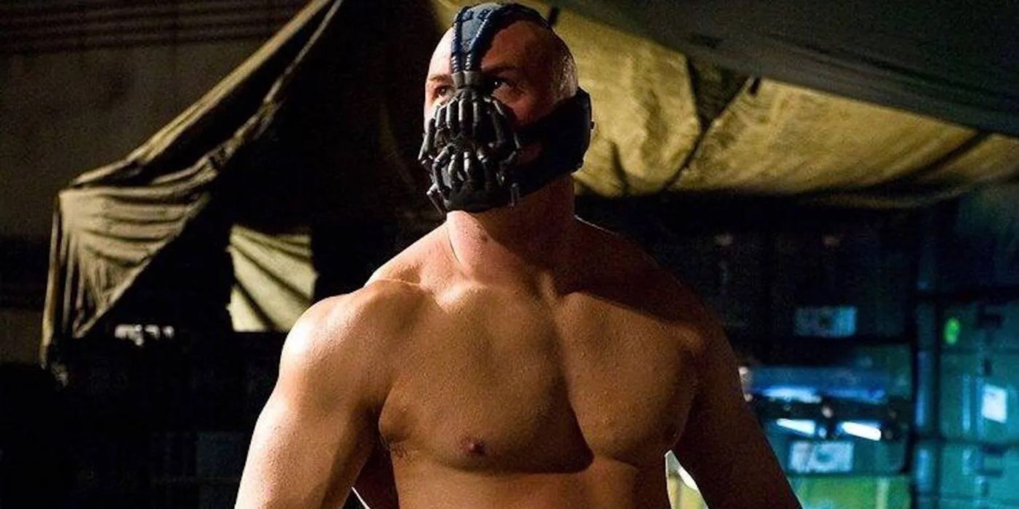 Bane shirtless and looking to the distance with a mask over his mouth in The Dark Knight Rises