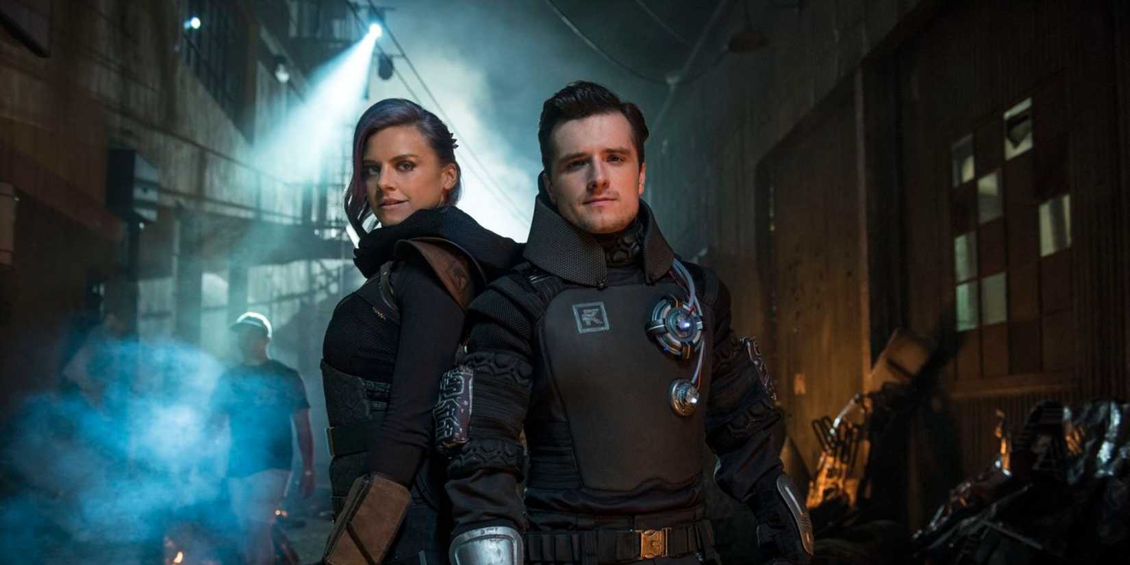Eliza Coupe and Josh Hutcherson in full Future Man soldier gear stand back-to-back and face the camera.