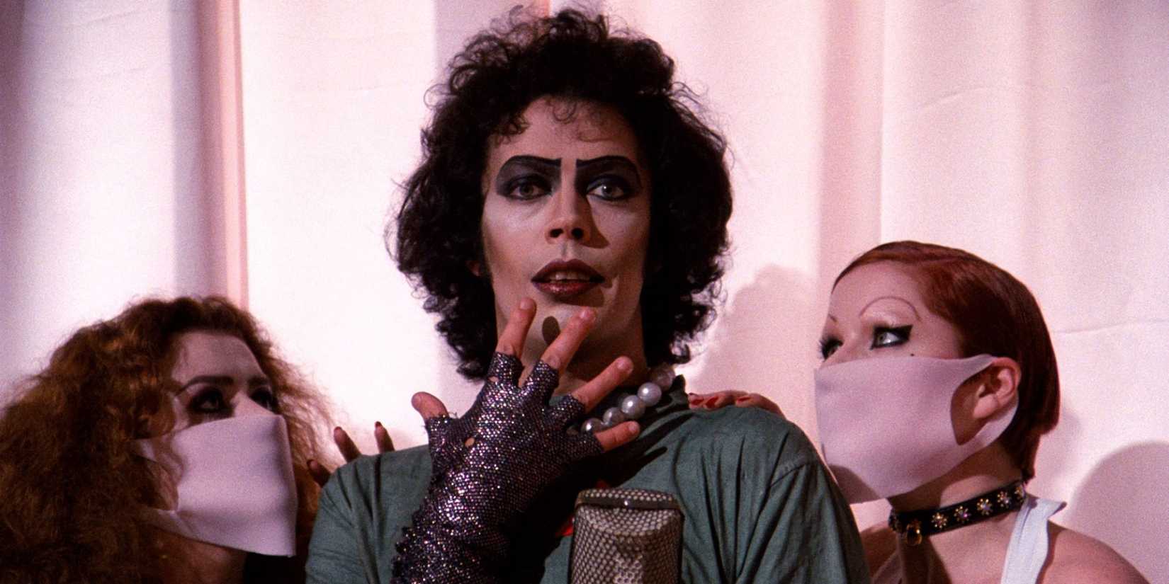Tim Curry as Frank-N-Furter in scrubs with Magenta and Columbia beside in The Rocky Horror Picture Show.