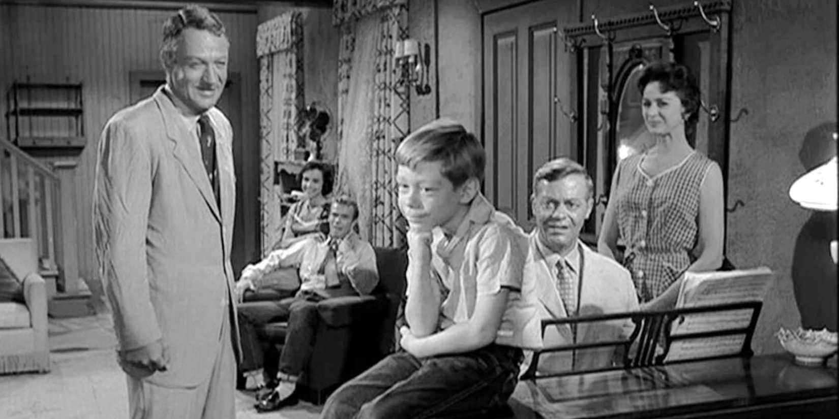 A family in a living room smiling, looking at a young boy in The Twilight Zone episode It's a Good Life.