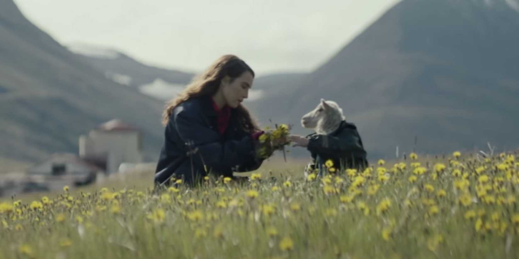 A woman and a small lamb sit among yellow flowers in Lamb.