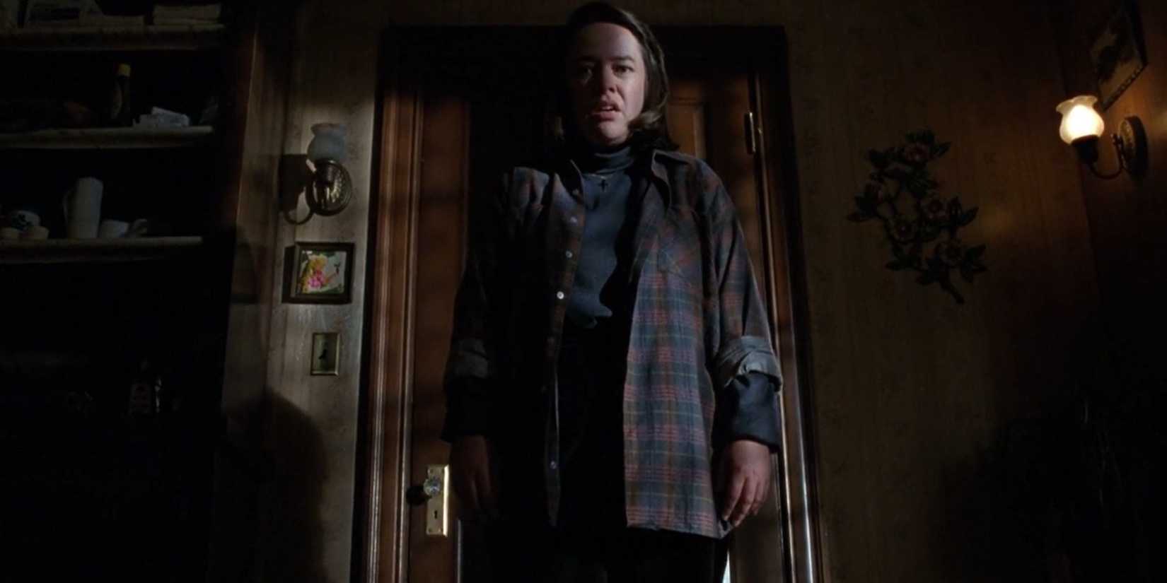 Annie Wilkes (Kathy Bates) standing in the shadows, enraged, in Misery (1990).