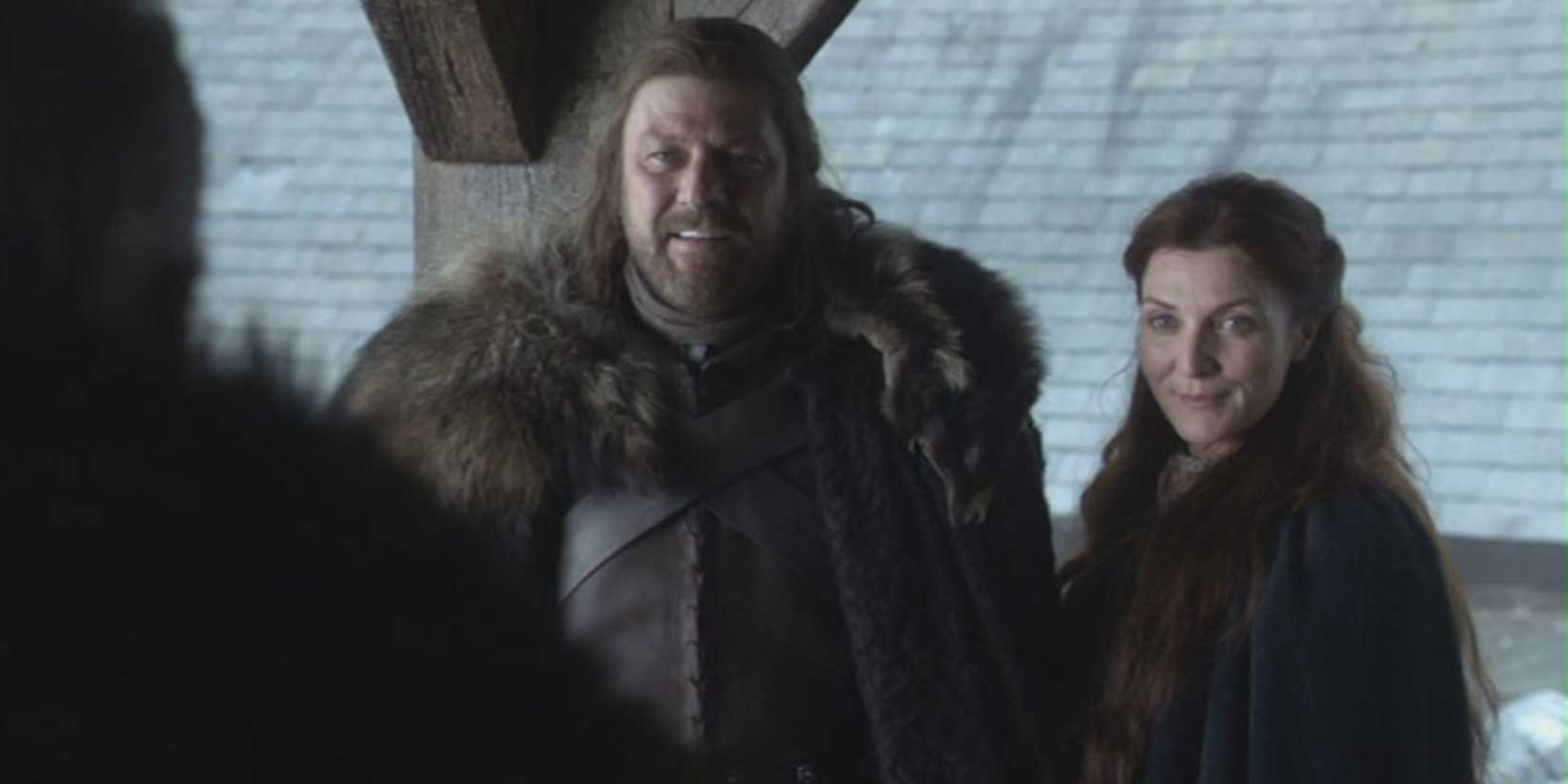 Sean Bean and Michelle Fairley in cloaks smiling at someone with their back to the camera in Game of Thrones.