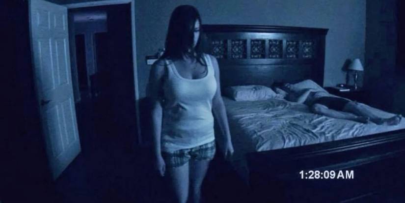 Katie standing and looking intently while Micah sleeps on the bed behind her in Paranormal Activity (2007)