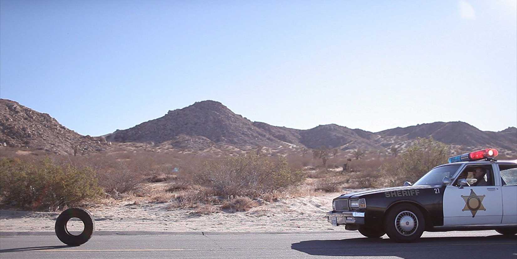a tire and a cop car heading toward each other on a desert highway