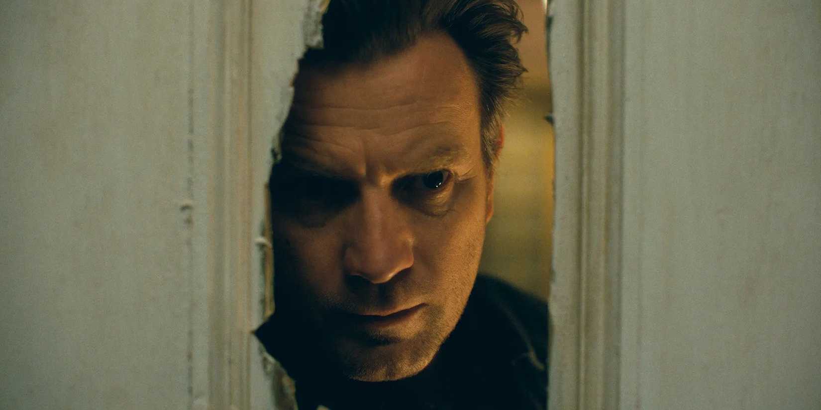 Ewan McGregor as Danny Torrence peeking through a broken door in Doctor Sleep