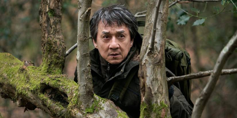Jackie Chan hiding in a forest and looking scared.