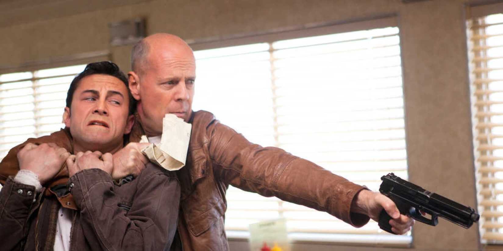 Bruce Willis holds a younger version of himself (Joseph Gordon Levitt) and aims a gun off camera