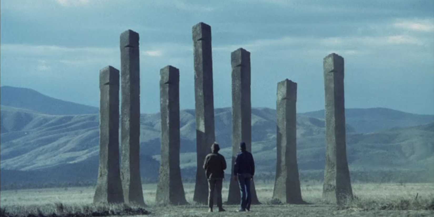 Two men standing before several rock pillars in phase iv0