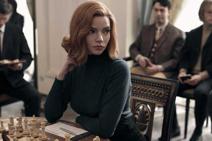 Anya Taylor-Joy as Beth Harmon, sitting in front of a chess board in The Queen's Gambit.