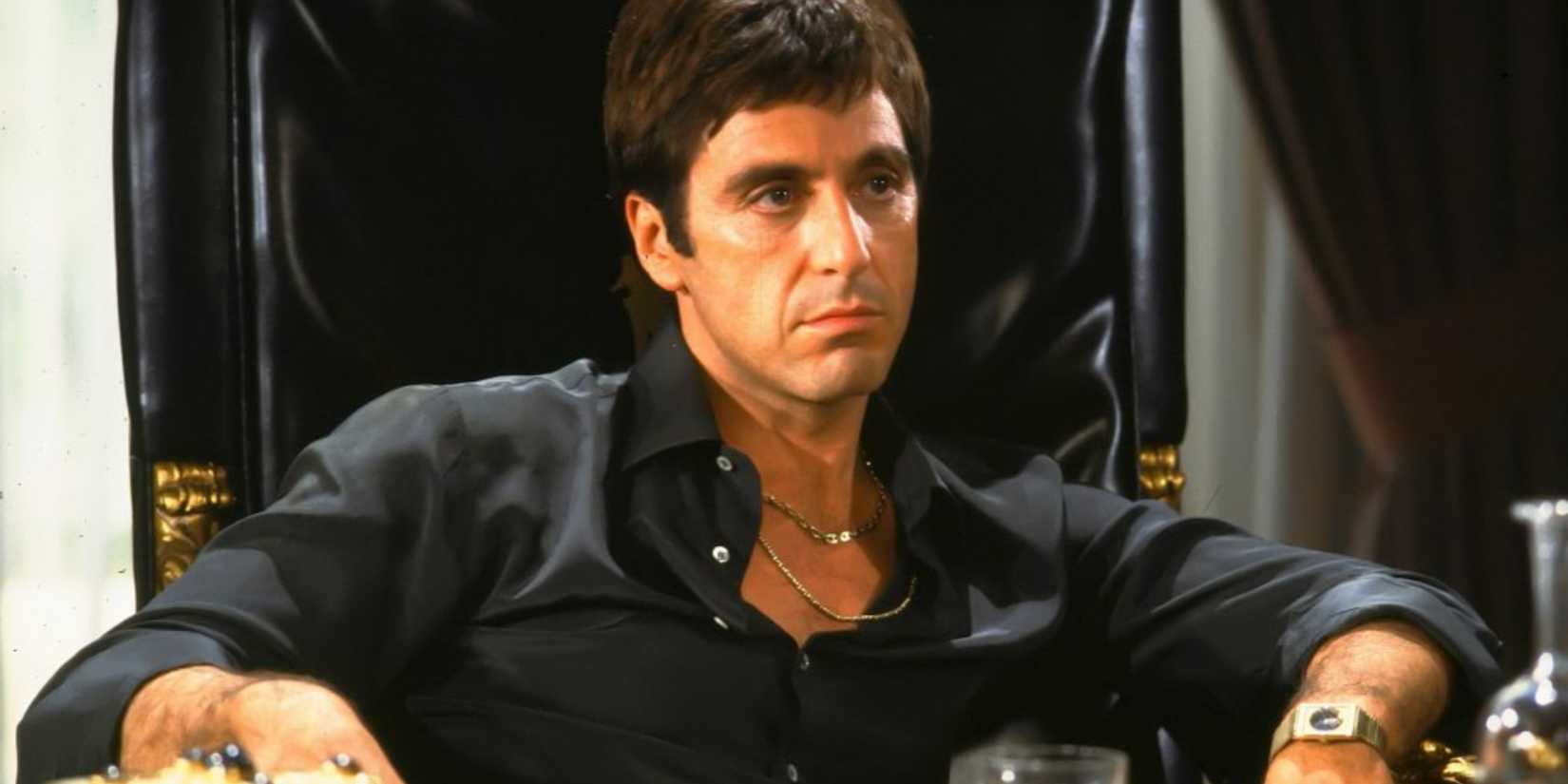 Al Pacino as Tony Montana sitting down and looking intently in Scarface.