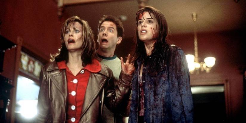 A bloodied Sidney Prescott stands with Gale and Randy in Scream, all looking shocked.