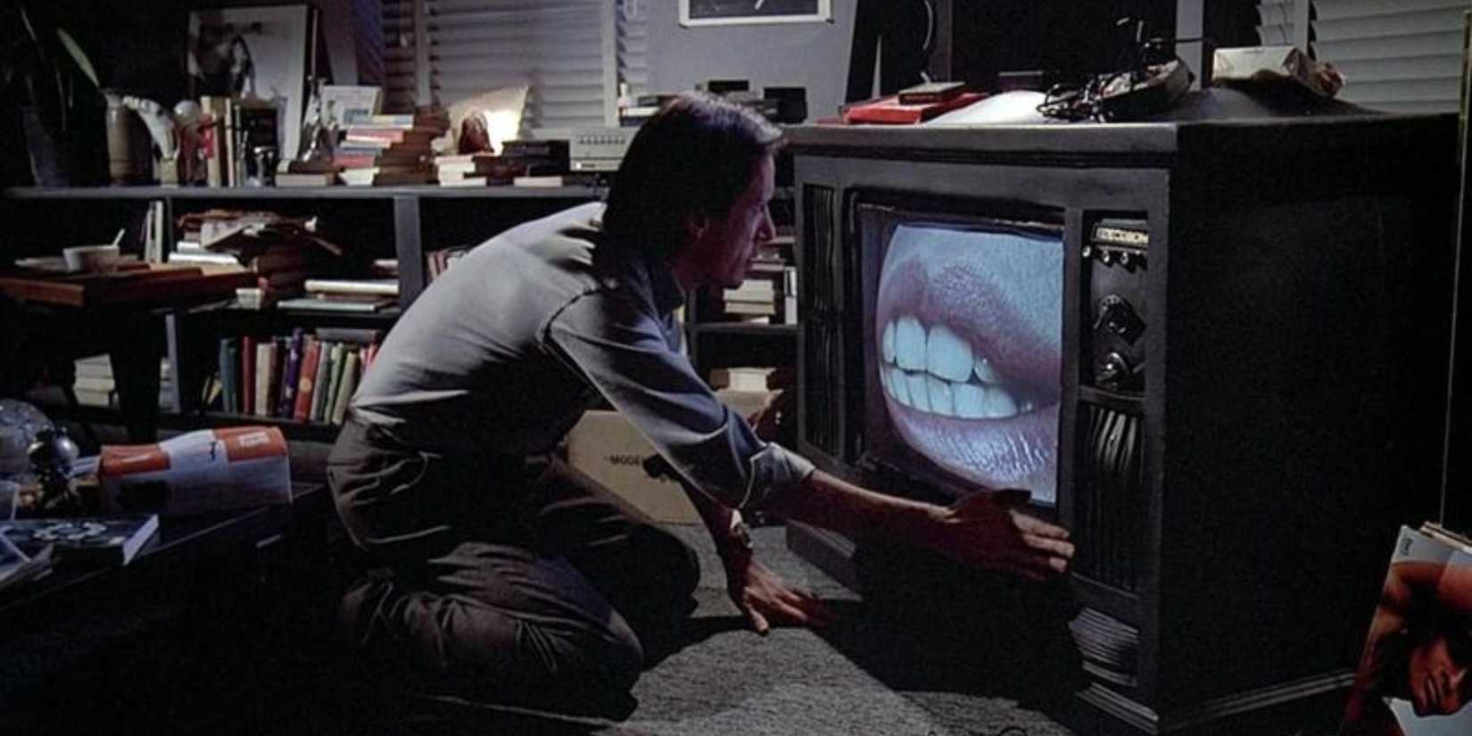 A man crouching in front of a TV set displaying an image of a woman's mouth