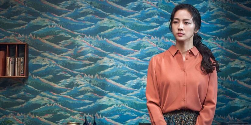 An emotional Tan Wei standing in front of a colorful wall in Decision to Leave