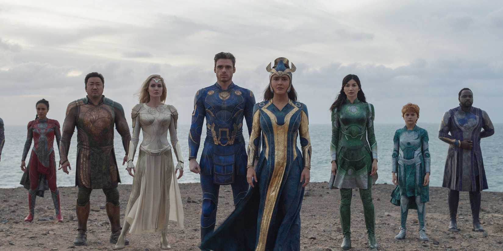 The cast stand together in their super hero outfits on a plateau in The Eternals.
