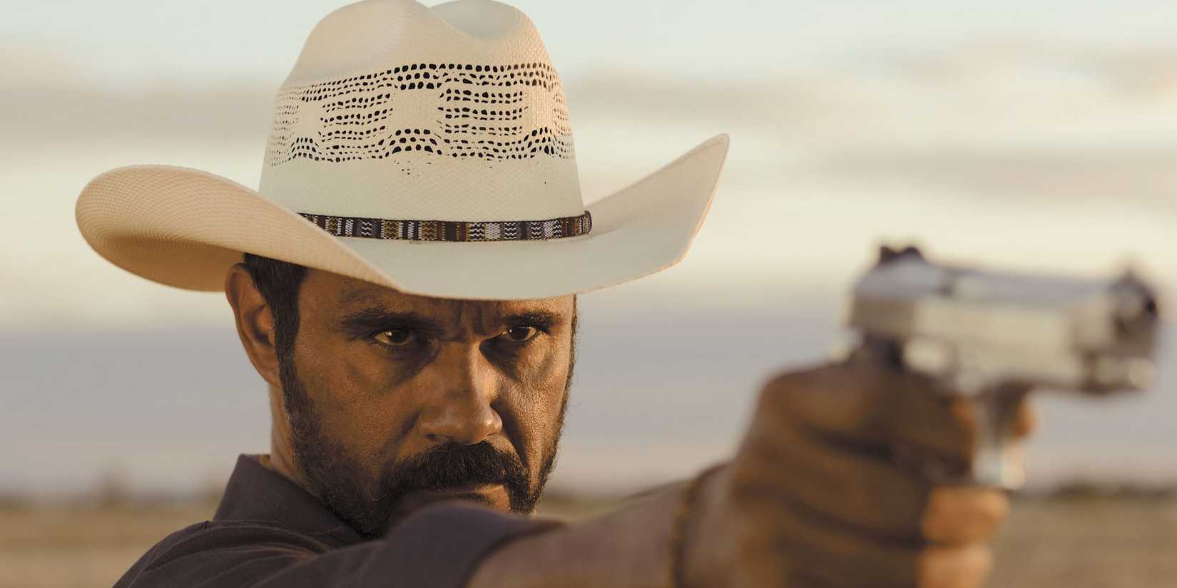 A man in a cowboy hat aiming a handgun in Mystery Road.