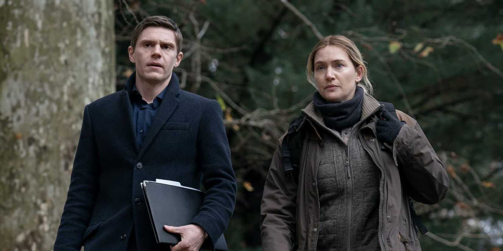 Evan Peters and Kate Winslet wearing coats, walking along side one another in 'Mare of Easttown'.