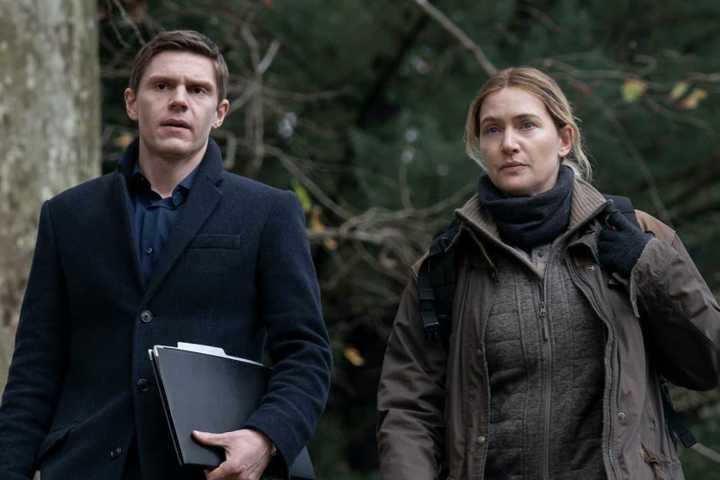 Evan Peters and Kate Winslet wearing coats, walking along side one another in 'Mare of Easttown'.