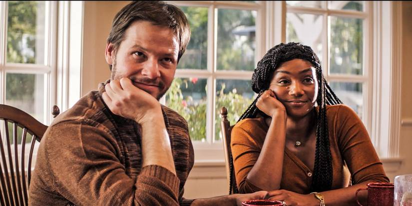 A man and a woman looking intently with ther chins resting on their hands in The Oath