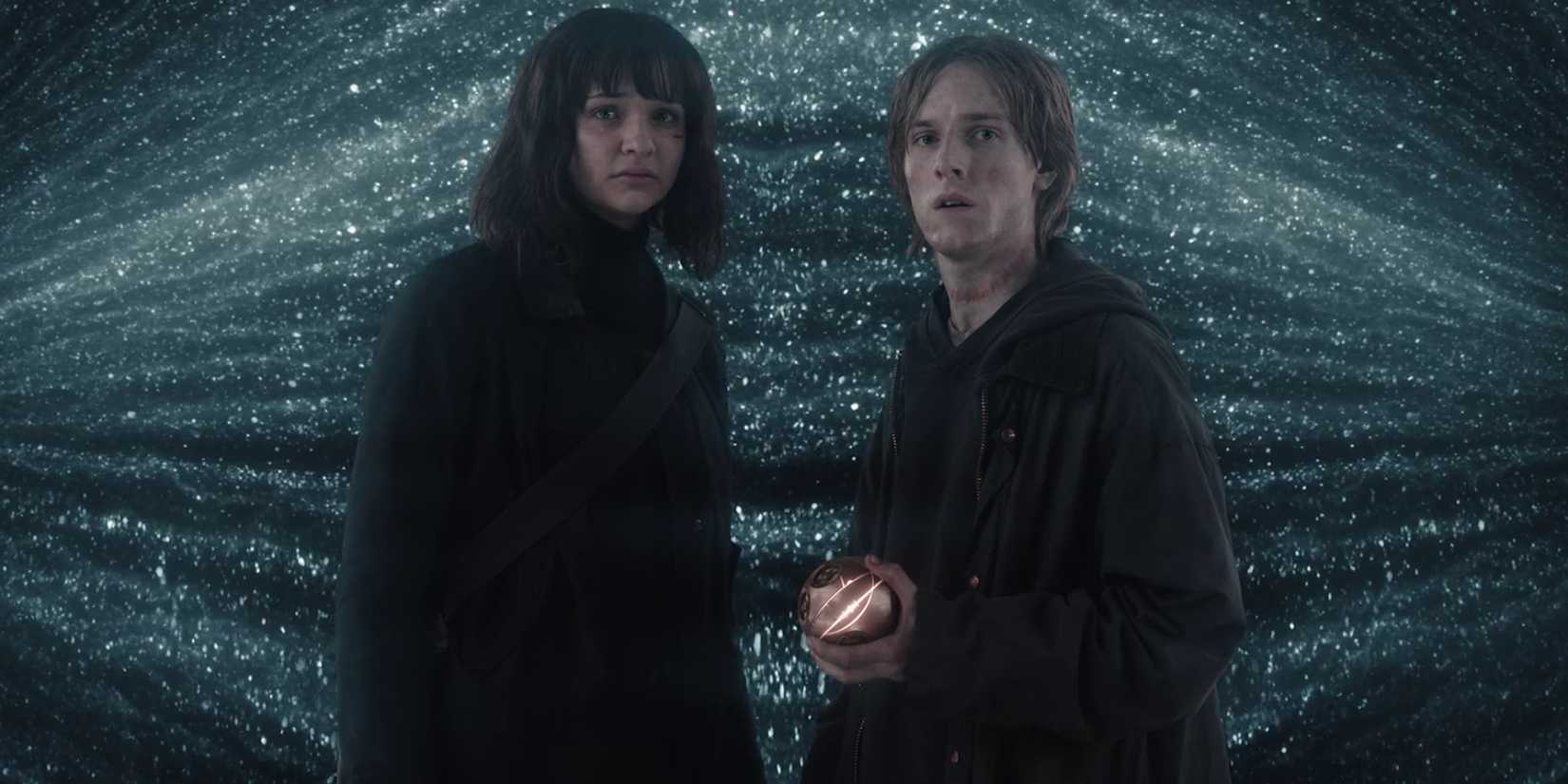 a man holding an orb, with a woman beside him, both in front of bright lights