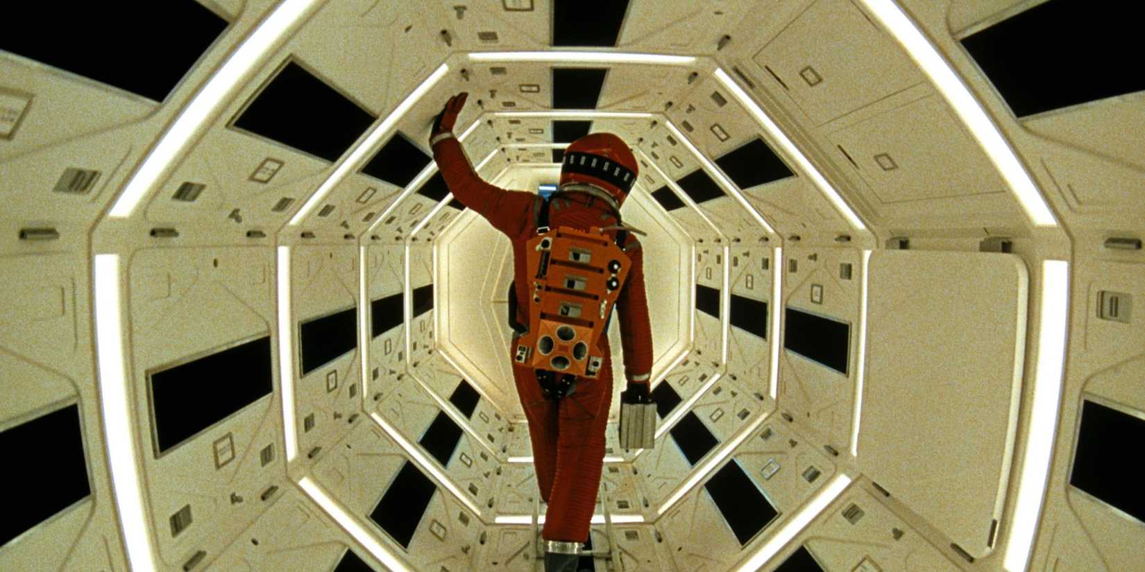Keir Dullea in a spacesuit walking through well-lit space pod in 2001: A Space Odyssey.
