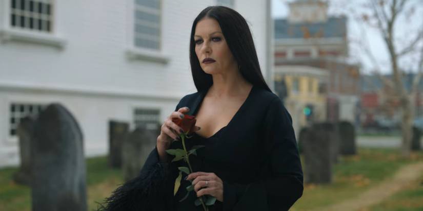 Catherine Zeta-Jones as Morticia Addams holding a rose standing by a grave in a cemetary in Wednesday (2022)