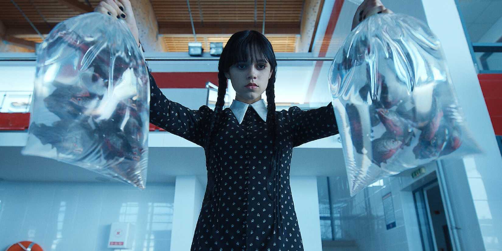 Jenna Ortega as Wednesday Addams holding bags of piranhas over a swimming pool